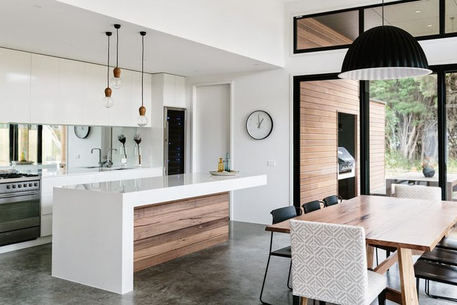 Phòng bếp tối giản màu trắng tinh tế và góc ăn hiện đại được kết nối bằng màu sắc và những chiếc đèn treo.